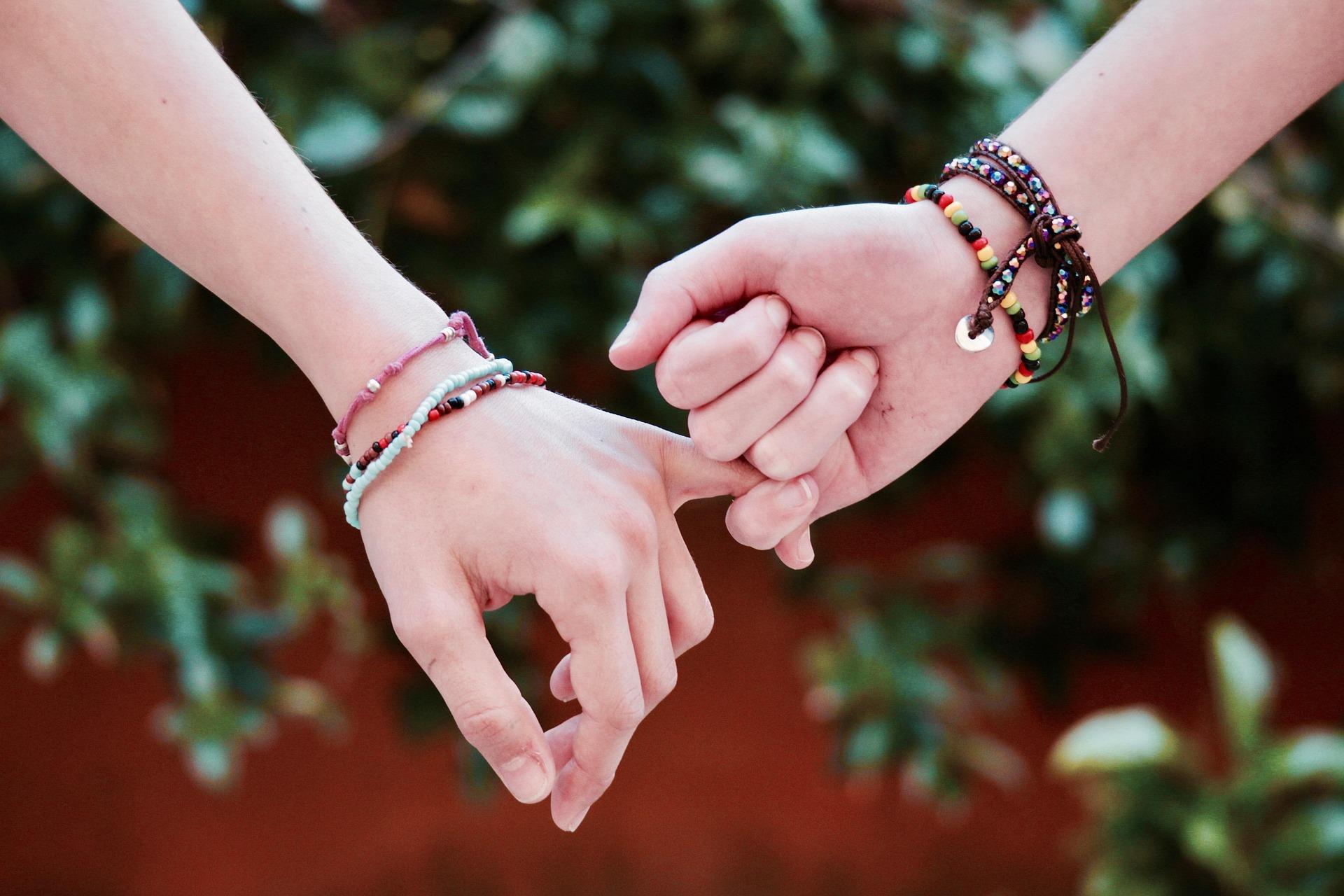 Two people's hands, linking little fingers with a garden in the background