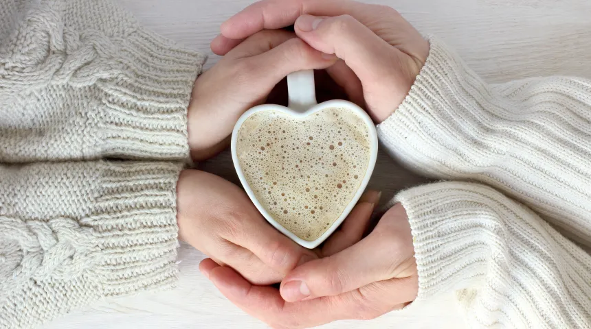 Two hands around a heart shaped mug filled with coffee