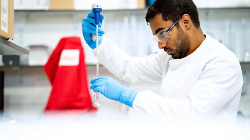 Image of a scientist in a lab coat in a laboratory, pouring a chemical into a test tube with a syringe 
