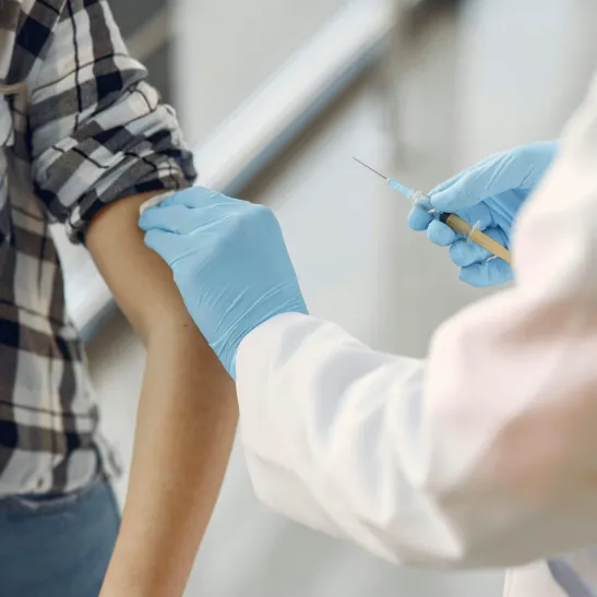 Healthcare professional wearing gloves giving a vaccination to a lady with rolled up sleeve. Only arms/torsos visible.